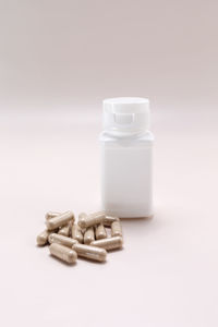 Close-up of pills spilling from bottle against white background