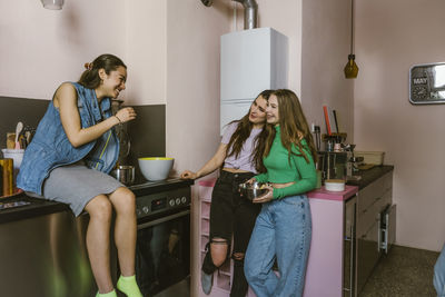 Smiling young female friends talking in kitchen at home