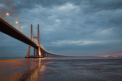 Bridge over sea against cloudy sky at dusk