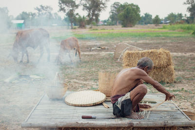 Shirtless senior man making straw basket