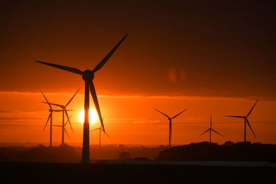 Windmills on silhouette landscape against sky during sunset