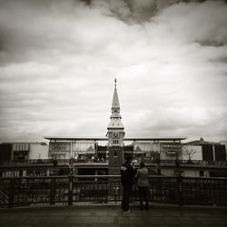 People walking in city against cloudy sky