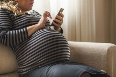 Midsection of woman using mobile phone while sitting on sofa
