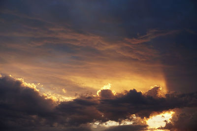 Low angle view of sunlight streaming through clouds during sunset