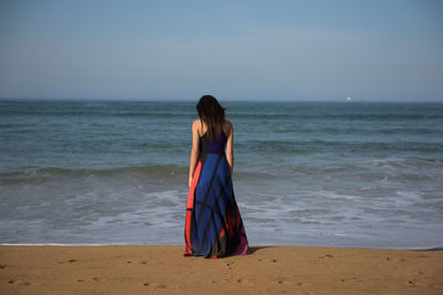 Rea view of young woman standing on shore at beach