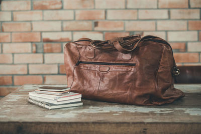 Books and leather on table against brick wall