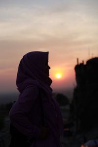 Midsection of woman standing against orange sky during sunset