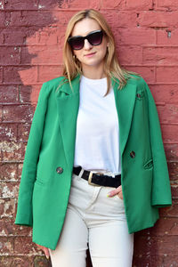 Young woman wearing sunglasses while standing against wall