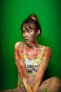 Portrait of young woman sitting against green background