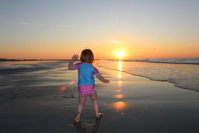 Girl standing on beach against clear sky during sunset