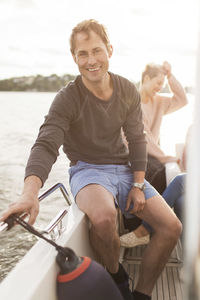 Portrait of happy man sitting on yacht with female friends in background