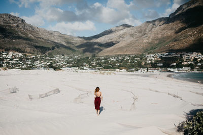 Rear view of woman walking at beach against mountain