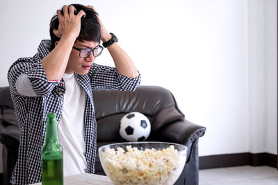 Sad young man with hand in hair sitting on sofa at home