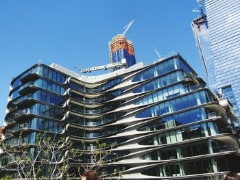 Low angle view of modern building in city against clear blue sky