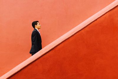 Side view of young man standing against orange wall