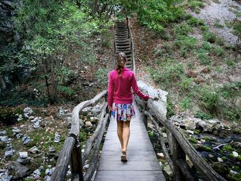 Rear view of young woman walking on a wooden bridge in the forest