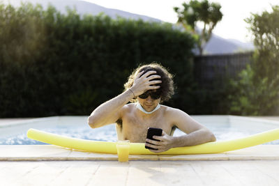 Young man using smart phone while standing in swimming pool