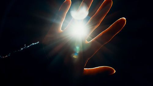 Close-up of hand against illuminated light against sky