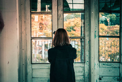 Rear view of woman looking through window
