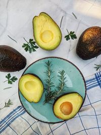 Fresh avocado with herbs and lemons lies on the table on blue plate on white background. flat lay.