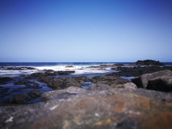 Scenic view of sea and rocks against clear blue sky