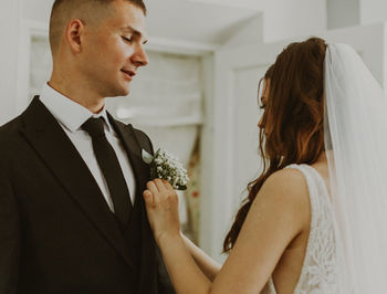 A beautiful bride inserts a bouquet of boutonnieres into the groom's jacket pocket.