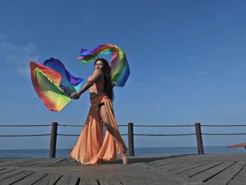 Woman with umbrella standing by railing against sky