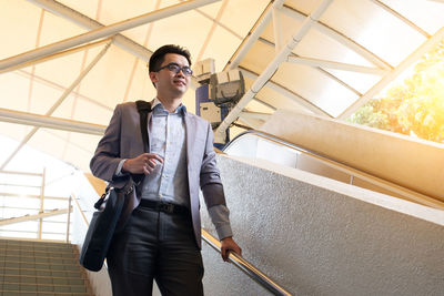 Low angle view of young man standing by railing