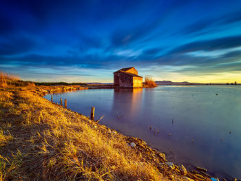 Buildings by lake against sky during sunset