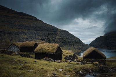 Old houses by sea and mountains against cloudy sky