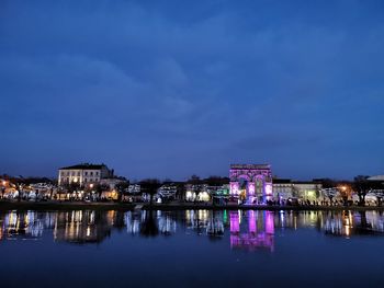 Illuminated buildings by river against sky at night