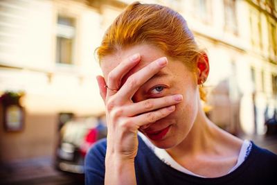 Close-up portrait of young woman with hand covering face standing on street