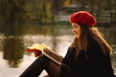 Woman in a red beret reading book on wooden pontoon. autumn season.