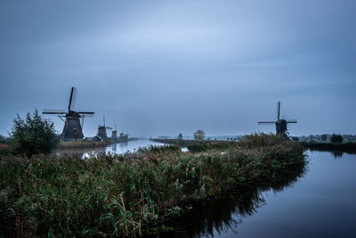 Traditional windmill by lake against sky