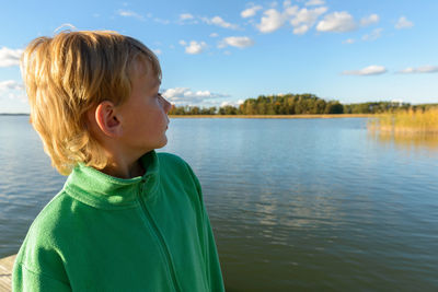 Portrait of boy looking at lake against sky