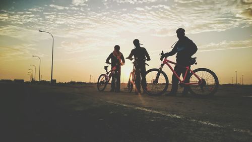 Low angle view of friends with bicycles standing on road during sunset