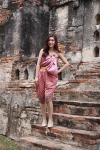 Portrait of a smiling young woman standing against stone wall