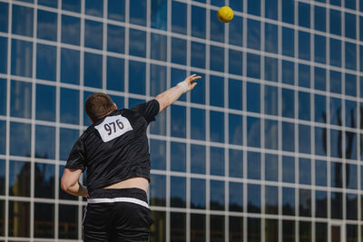 Male athlete shot put on background glass facade