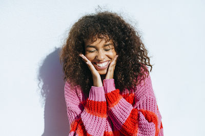 Portrait of laughing young woman with curly hair against white wall