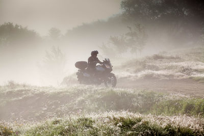 Man riding motorcycle on field against sky during sunset