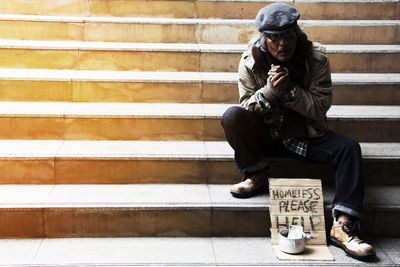 Beggar with text on cardboard sitting on steps