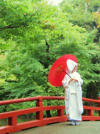 Woman with red umbrella against trees