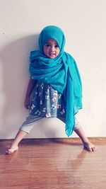 Portrait of cute girl wearing blue headscarf while standing against white wall