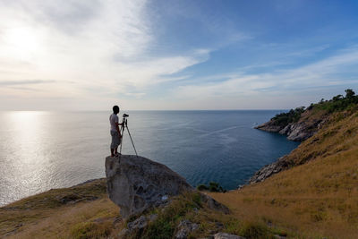 Men standing on rock by sea against sky