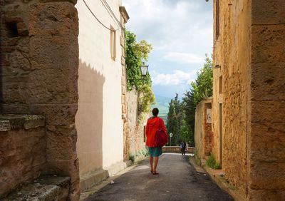 Rear view of woman walking on alley amidst buildings