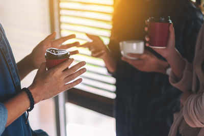 Midsection of people holding disposable coffee cup while discussing in office