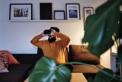 Man photographing on sofa at home