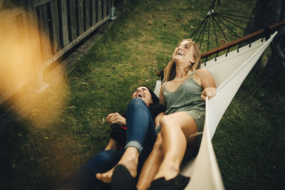 High angle view of cheerful female friends with lying on hammock at yard