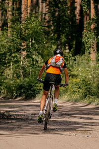 Back young cyclist with backpack and helmet biking on forest trail