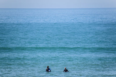 Rear view of surfers in sea against sky